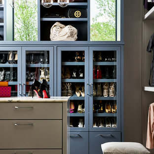Immagine di una cabina armadio per donna contemporanea con ante di vetro, ante blu e parquet scuro