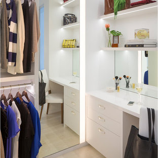 Cette image montre un grand dressing design pour une femme avec un placard à porte plane, des portes de placard blanches et un sol en bois clair.