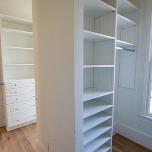 Modelo de armario vestidor unisex, de estilo de casa de campo, grande, con armarios abiertos, puertas de armario blancas, suelo de madera clara y suelo marrón
