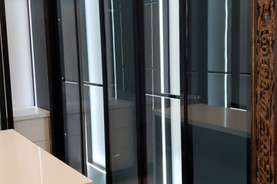 Foto de armario y vestidor unisex minimalista de tamaño medio con a medida, armarios tipo vitrina, puertas de armario negras, suelo de madera clara y suelo marrón