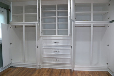 Diseño de armario vestidor unisex actual grande con armarios con paneles empotrados, puertas de armario blancas y suelo de madera en tonos medios