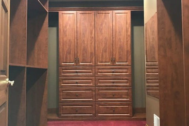 Imagen de armario vestidor unisex clásico grande con armarios con paneles con relieve, puertas de armario de madera en tonos medios, moqueta y suelo rojo