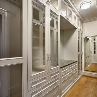 Cette photo montre un grand dressing chic neutre avec un placard avec porte à panneau encastré, des portes de placard grises et un sol en bois clair.