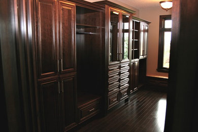 Example of a classic dark wood floor and brown floor reach-in closet design in Edmonton with raised-panel cabinets and brown cabinets