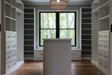 Inspiration for a mid-sized farmhouse medium tone wood floor walk-in closet remodel in Baltimore with shaker cabinets and white cabinets