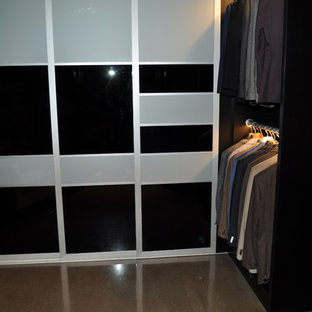 Modelo de vestidor de hombre, minimalista, pequeño, con armarios con paneles lisos, puertas de armario negras, suelo de cemento y suelo gris