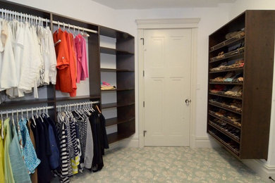 Large gender neutral wardrobe in New York with dark wood cabinets and carpet.