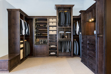 Large modern walk-in wardrobe for men in Minneapolis with recessed-panel cabinets, dark wood cabinets, carpet and beige floors.