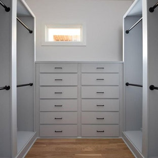 Modelo de vestidor unisex, minimalista, de tamaño medio, con armarios con rebordes decorativos, puertas de armario blancas, suelo de madera en tonos medios y suelo beige