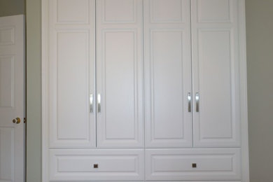 Imagen de vestidor unisex actual pequeño con puertas de armario blancas, suelo de madera en tonos medios y armarios con paneles con relieve