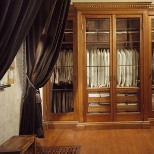 Ejemplo de armario vestidor unisex, ecléctico, extra grande, con armarios tipo vitrina, puertas de armario de madera oscura y suelo de madera en tonos medios