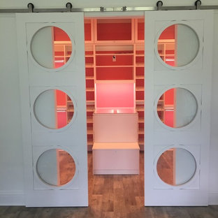 Immagine di una grande cabina armadio per donna moderna con ante con bugna sagomata, ante bianche, pavimento in vinile e pavimento marrone