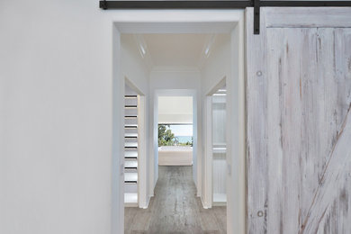 Example of a mid-sized beach style gender-neutral light wood floor and brown floor walk-in closet design in Orange County with glass-front cabinets and white cabinets
