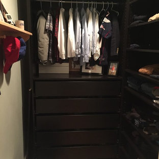 Foto de armario vestidor de hombre, actual, con armarios con paneles lisos, puertas de armario negras y suelo de madera en tonos medios