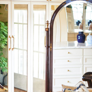 Inspiration för mycket stora klassiska walk-in-closets för kvinnor, med luckor med glaspanel, vita skåp och mellanmörkt trägolv