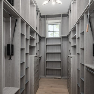 Diseño de armario vestidor de mujer y abovedado, moderno, grande, con armarios con paneles lisos, puertas de armario grises, suelo de madera clara y suelo beige