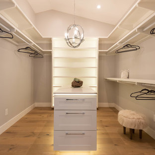 Cette image montre un dressing minimaliste de taille moyenne et neutre avec un placard à porte shaker, des portes de placard blanches et un sol en bois brun.