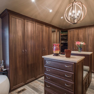 Ispirazione per una grande cabina armadio unisex chic con ante con bugna sagomata, ante in legno scuro, pavimento in compensato e pavimento marrone
