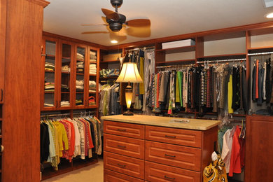 Example of a large carpeted walk-in closet design in Other with raised-panel cabinets and medium tone wood cabinets