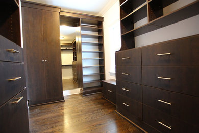 Diseño de armario vestidor de hombre minimalista grande con armarios con paneles lisos, puertas de armario de madera en tonos medios, suelo de madera oscura y suelo marrón