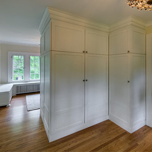 Diseño de vestidor unisex, romántico, con armarios estilo shaker, puertas de armario blancas y suelo de madera en tonos medios