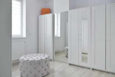 Small scandi gender neutral walk-in wardrobe with recessed-panel cabinets, white cabinets, light hardwood flooring and beige floors.
