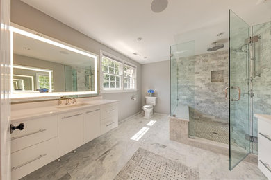 Réalisation d'une salle de bain minimaliste de taille moyenne avec WC séparés, mosaïque, un mur gris, un lavabo encastré, un plan de toilette en surface solide, un placard à porte plane, des portes de placard blanches et un sol en bois brun.