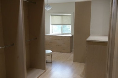 Ejemplo de armario vestidor unisex actual grande con armarios con paneles lisos, puertas de armario de madera clara, suelo de madera clara y suelo beige