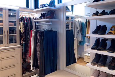 Modelo de vestidor de mujer moderno grande con armarios con paneles lisos, puertas de armario de madera clara y suelo de madera en tonos medios