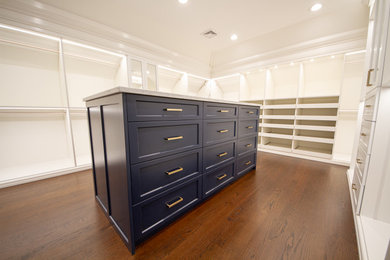 Diseño de armario vestidor unisex tradicional grande con armarios con paneles empotrados, puertas de armario azules y suelo de madera oscura