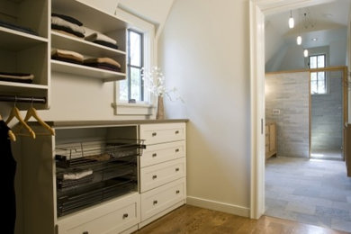 Example of a large trendy gender-neutral light wood floor walk-in closet design in Other with shaker cabinets and white cabinets