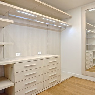 Diseño de armario vestidor unisex, minimalista, grande, con armarios con paneles lisos, puertas de armario de madera clara y suelo de madera en tonos medios