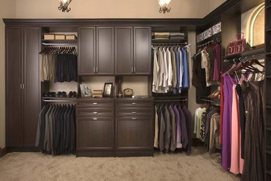 Large gender-neutral carpeted walk-in closet photo in Phoenix with dark wood cabinets