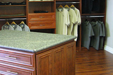 Modelo de armario vestidor unisex tradicional grande con armarios con paneles empotrados, puertas de armario de madera oscura y suelo de madera en tonos medios