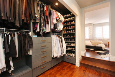 Example of a large minimalist gender-neutral medium tone wood floor and brown floor walk-in closet design in New York with flat-panel cabinets and gray cabinets