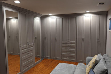 Diseño de armario vestidor unisex tradicional grande con armarios con rebordes decorativos, puertas de armario grises y suelo de madera en tonos medios