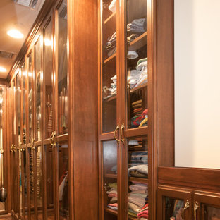 Immagine di una cabina armadio unisex mediterranea di medie dimensioni con ante di vetro, ante in legno scuro e pavimento in legno massello medio