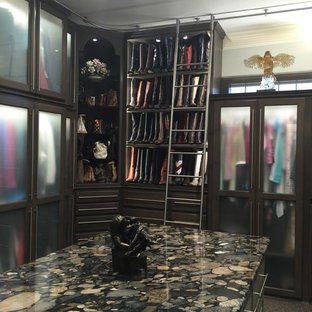 Esempio di una grande cabina armadio unisex tradizionale con ante di vetro, ante in legno scuro, moquette e pavimento marrone