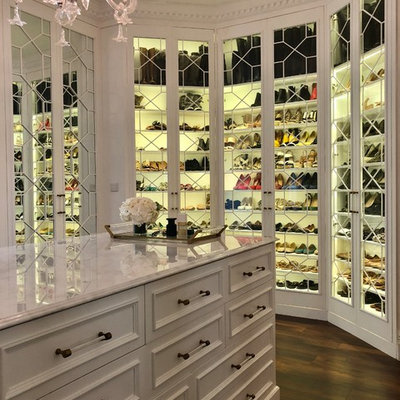 Example of a transitional dark wood floor and brown floor walk-in closet design in Other with glass-front cabinets and white cabinets