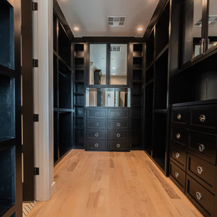 Imagen de armario vestidor unisex, moderno, grande, con puertas de armario negras y suelo de madera clara
