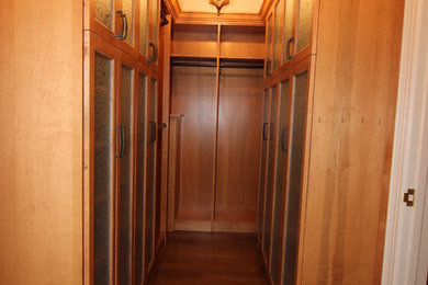 Example of a large classic walk-in closet design in Other with glass-front cabinets and medium tone wood cabinets