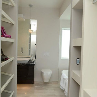 Modelo de armario y vestidor minimalista, grande, con armarios con paneles lisos, puertas de armario de madera en tonos medios y suelo de travertino