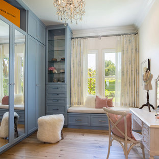 Imagen de vestidor de mujer, clásico renovado, con armarios estilo shaker, puertas de armario azules, suelo de madera en tonos medios y suelo marrón