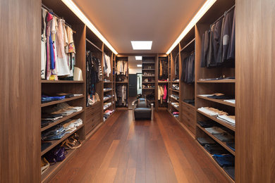 Imagen de vestidor unisex actual grande con armarios con paneles lisos, puertas de armario de madera oscura, suelo de madera en tonos medios y suelo marrón