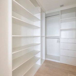 Ejemplo de armario vestidor unisex, moderno, grande, con armarios con paneles lisos, puertas de armario blancas, suelo de baldosas de porcelana y suelo beige