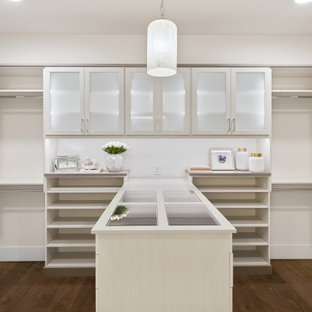 Foto di una grande cabina armadio unisex stile americano con ante di vetro, ante in legno chiaro, pavimento in legno massello medio e pavimento marrone