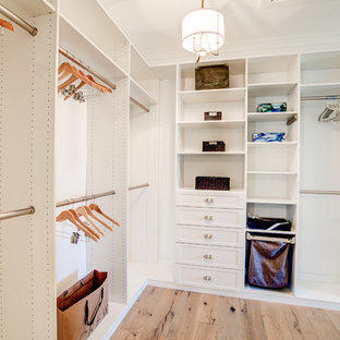 Modelo de armario vestidor unisex, de estilo de casa de campo, extra grande, con armarios con paneles empotrados, puertas de armario blancas, suelo de madera clara y suelo marrón