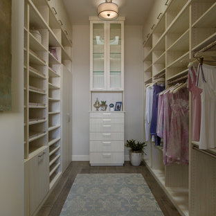 Modelo de armario vestidor de mujer, clásico renovado, de tamaño medio, con armarios con paneles lisos, puertas de armario de madera clara, suelo de madera oscura y suelo marrón