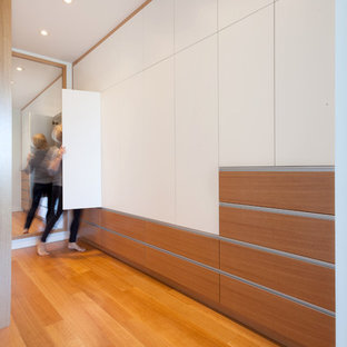 Diseño de armario vestidor unisex, minimalista, de tamaño medio, con armarios con paneles lisos, puertas de armario blancas y suelo de madera clara