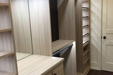 Ejemplo de armario vestidor unisex clásico renovado de tamaño medio con armarios con paneles lisos, puertas de armario de madera clara, suelo de madera oscura y suelo marrón